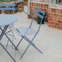 Blue bistro table and chairs on the paving beside the greenhouse