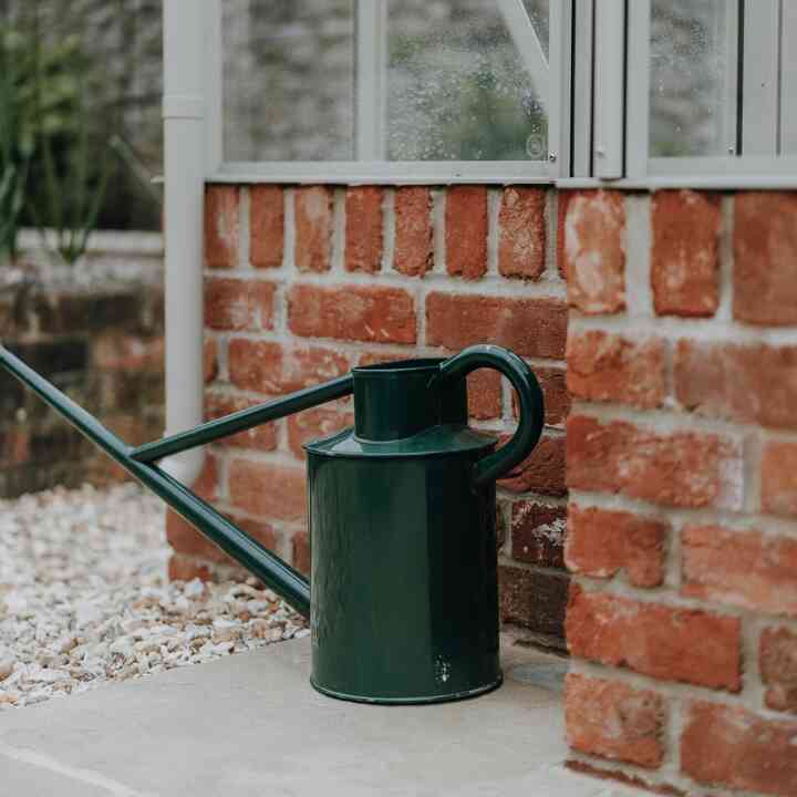 Green watering can on the paving beside the greenhouse brick base