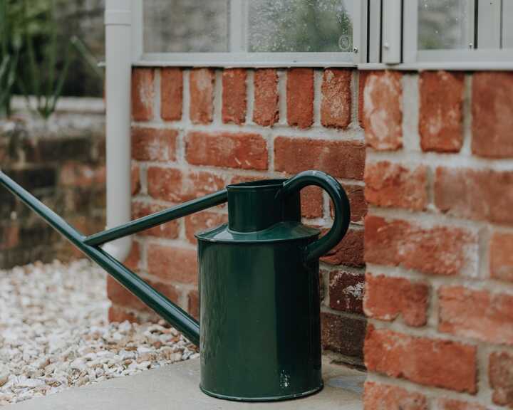 Green watering can on the paving beside the greenhouse brick base