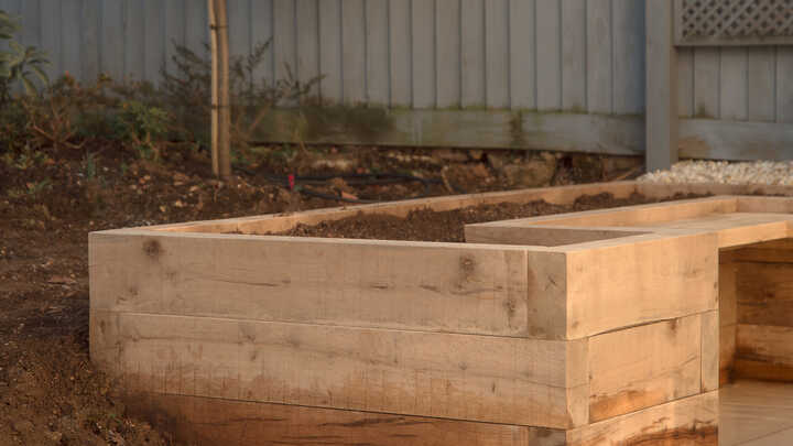 Garden with raised planter beds, green grass, and trees under a cloudy sky.