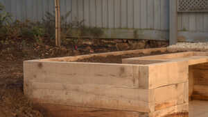 Garden with raised planter beds, green grass, and trees under a cloudy sky.