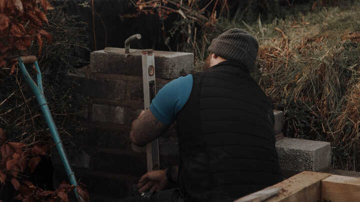 Garden with raised planter beds, green grass, and trees under a cloudy sky.