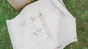 Garden with raised planter beds, green grass, and trees under a cloudy sky.