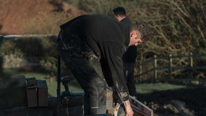 Garden with raised planter beds, green grass, and trees under a cloudy sky.