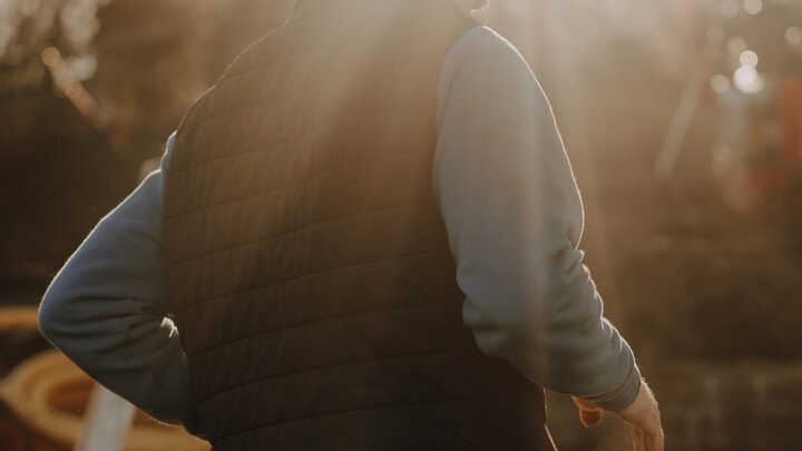 A glass greenhouse with plants, adjacent to a stone path and house, under a cloudy sky.