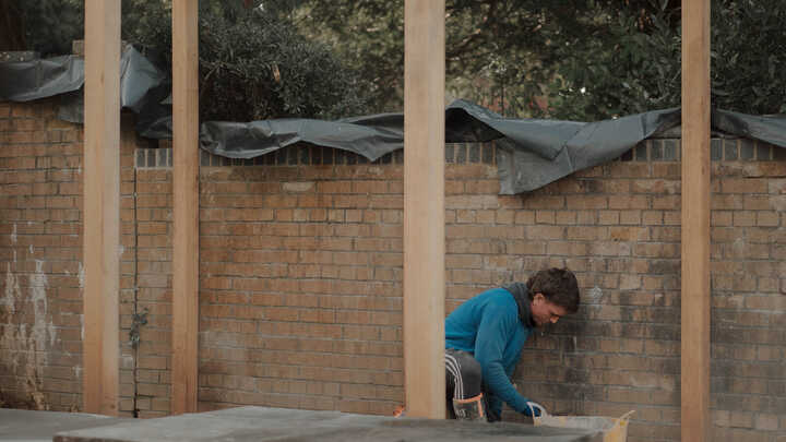 Garden with raised planter beds, green grass, and trees under a cloudy sky.
