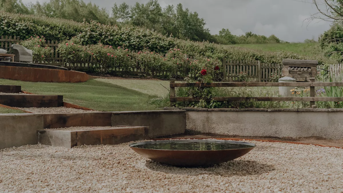 Corten steel water bowl on a gravel seating area with terraced lawns, sleeper steps and countryside views in a Somerset garden