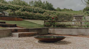 Corten steel water bowl on a gravel seating area with terraced lawns, sleeper steps and countryside views in a Somerset garden