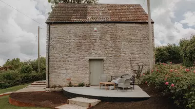 New paved terrace beside a stone outbuilding with seating and rose planting after landscaping