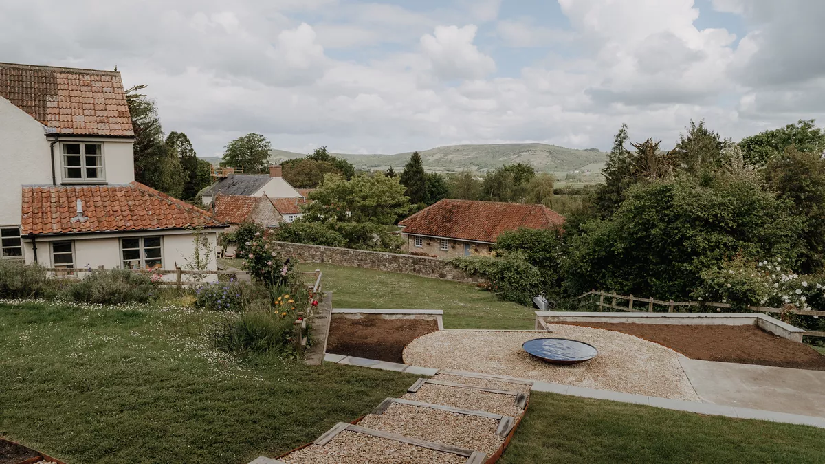 Elevated view of a landscaped sloping garden with gravel terrace, water bowl and countryside views, Somerset