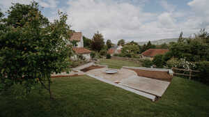 Elevated view of a terraced Somerset country garden with lawns, a gravel seating area and water bowl, and village rooftops beyond