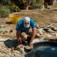Sibley Landscapes team member crouching to fit stones around the filled pond liner