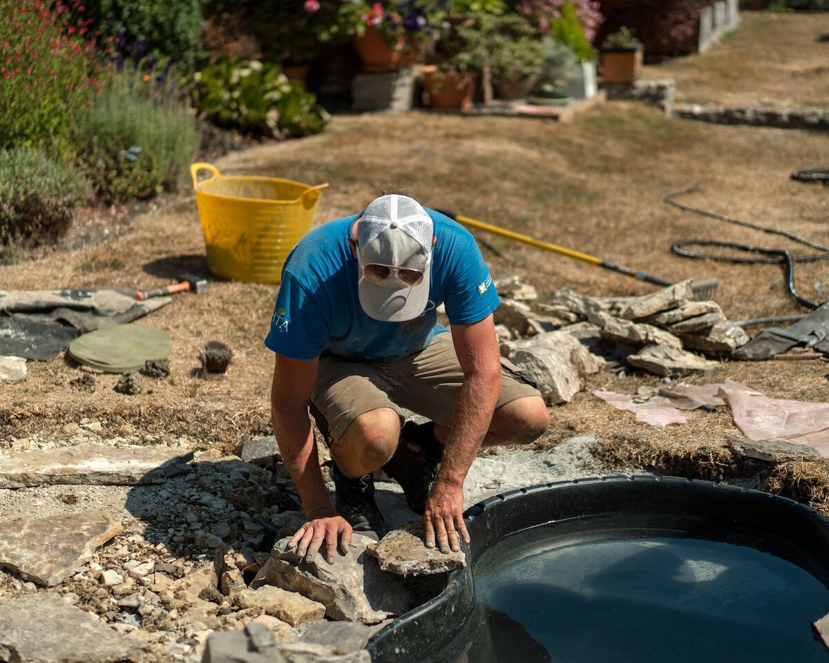 Sibley Landscapes team member crouching to fit stones around the filled pond liner