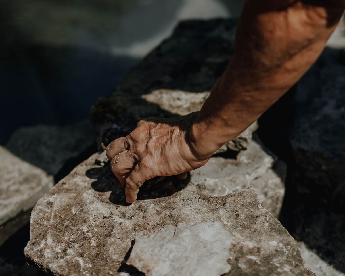 Hand pressing a flat stone into place on the pond edge
