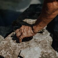 Hand pressing a flat stone into place on the pond edge