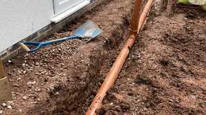 Orange drainage pipe laid in a trench alongside a house wall before the ground is reinstated