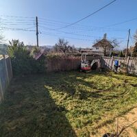 A sunny garden with grass, a fence, and a small tractor in the corner.