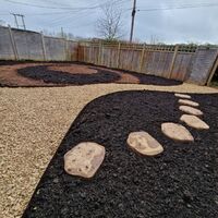 Garden with gravel paths, stepping stones, and mulched areas, enclosed by a wooden fence.