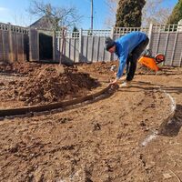 Sibley worker shapes soil in a garden, with tools and a fence in the background.