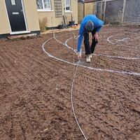 Sibley Landscapes team marking circles in muddy garden soil near a house.