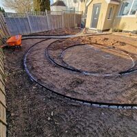 Construction area with circular outlines in dirt, a wheelbarrow, and a house in the background.