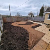 A garden area with a curved path in sandy soil and a paved patio.