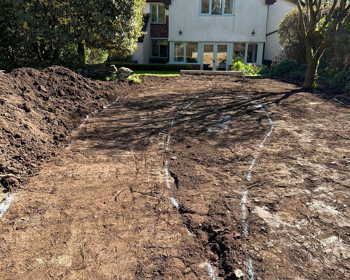 A cleared dirt area in front of a house surrounded by trees and blue sky.