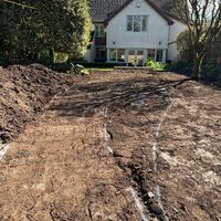 A cleared dirt area in front of a house surrounded by trees and blue sky.