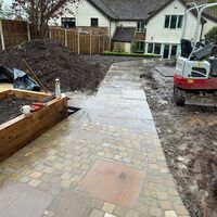 Paved pathway leading to a house, with construction materials and a machine in the background.