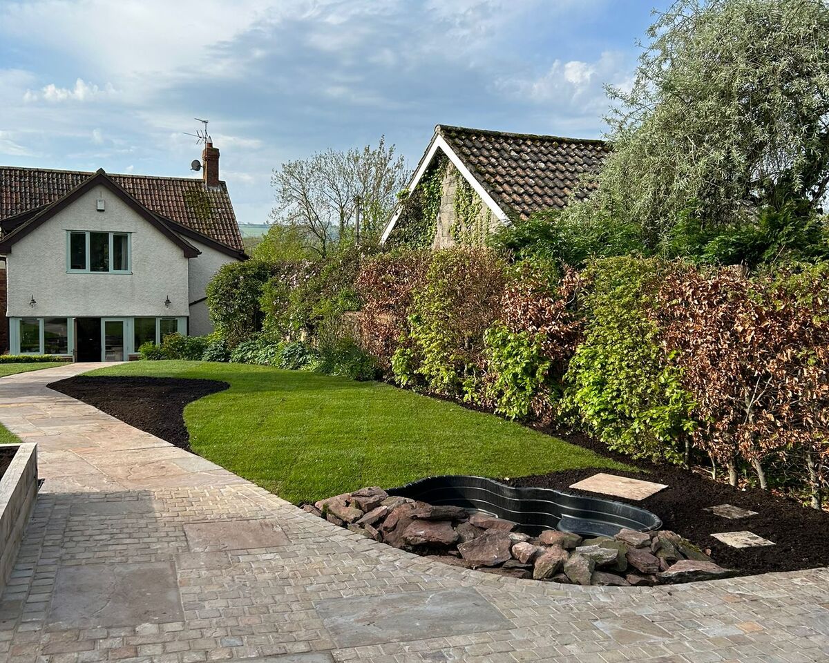 A landscaped garden featuring stone paths, green grass, and two houses in the background.