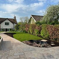 A landscaped garden featuring stone paths, green grass, and two houses in the background.