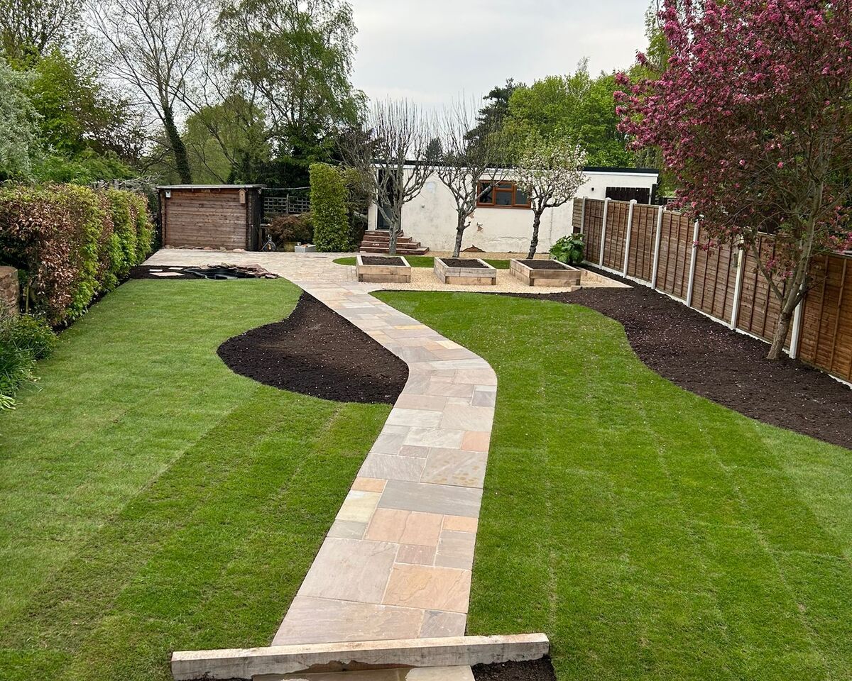 A landscaped garden featuring a stone pathway, grass, and decorative trees.