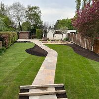 A landscaped garden featuring a stone pathway, grass, and decorative trees.