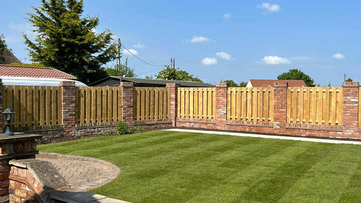 Lawn area with trimmed grass and wooden fences under a clear blue sky.