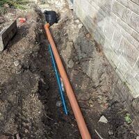 A trench with a large, orange pipe running alongside a gray wall.