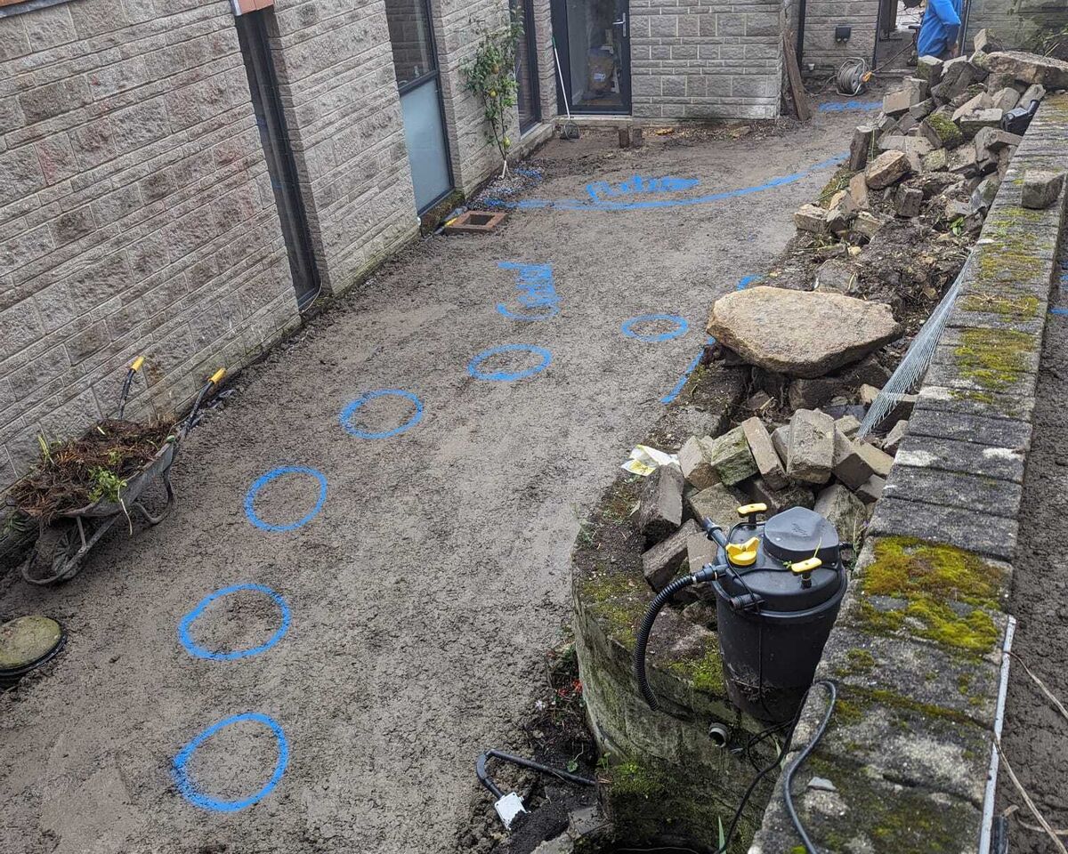 A garden area with stone walls, a pond, and a pathway decorated with blue flowers.