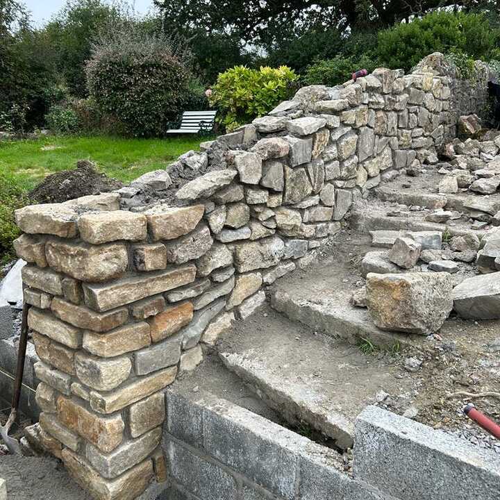 Stone wall under construction next to a set of stone steps in a garden setting.