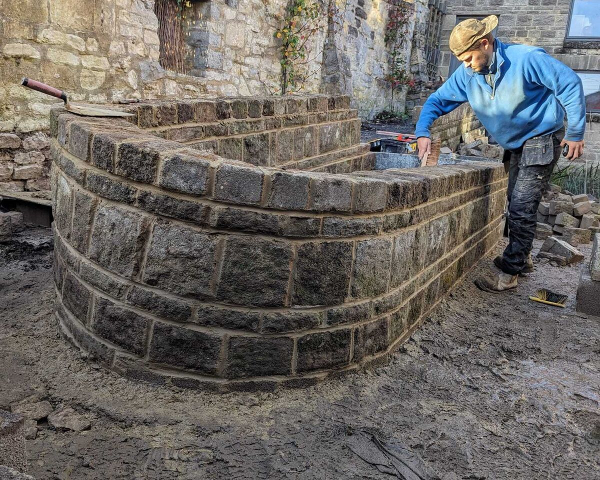 A person builds a curved stone wall in a construction area.