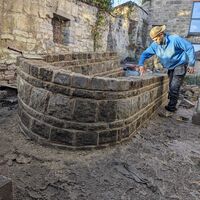 A person builds a curved stone wall in a construction area.
