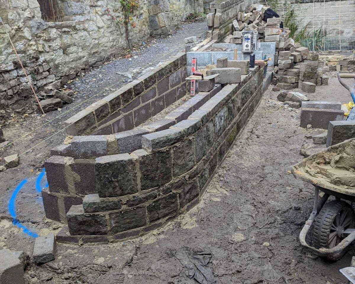 Construction site with a stone wall partially built in a rocky environment.