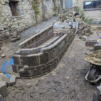 Construction site with a stone wall partially built in a rocky environment.