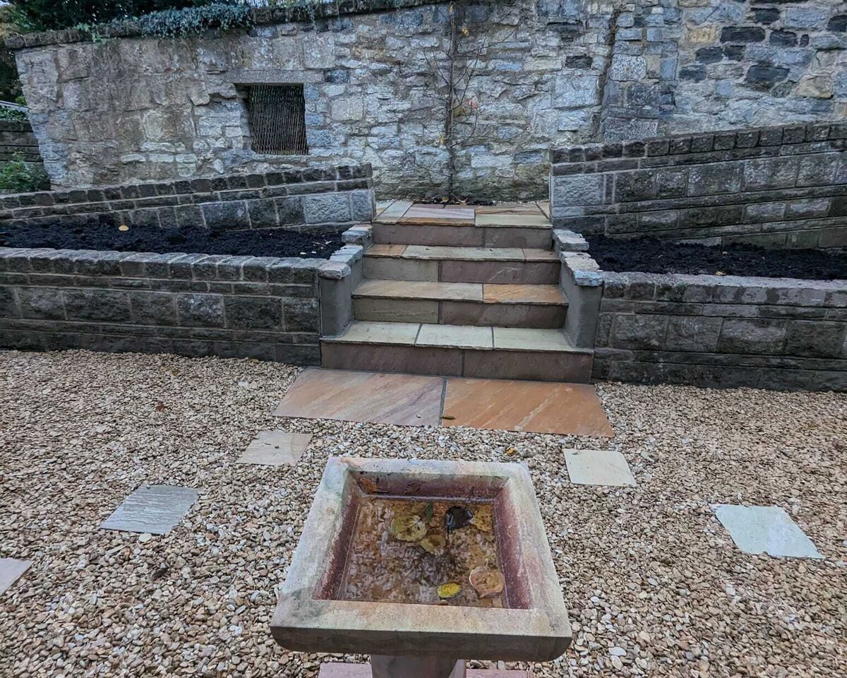 Stone steps lead up to a walled garden with a decorative stone planter in the foreground.