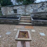 Stone steps lead up to a walled garden with a decorative stone planter in the foreground.