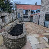 A stone courtyard with raised beds and a mix of paving stones under a cloudy sky.