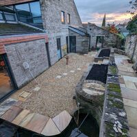 Modern stone building with a gravel garden, pond, and landscaped areas at sunset.