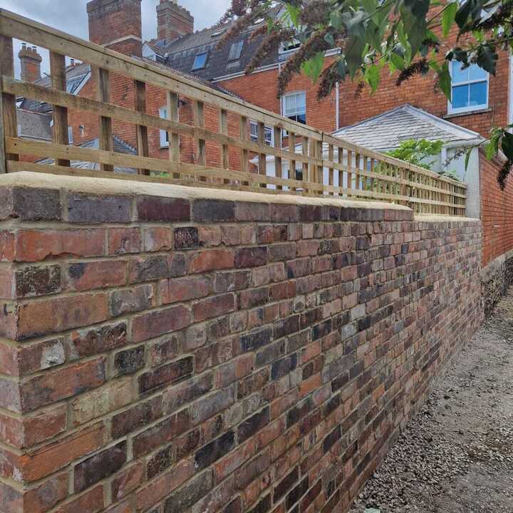 Brick wall topped with wooden lattice, with buildings and trees in the background.