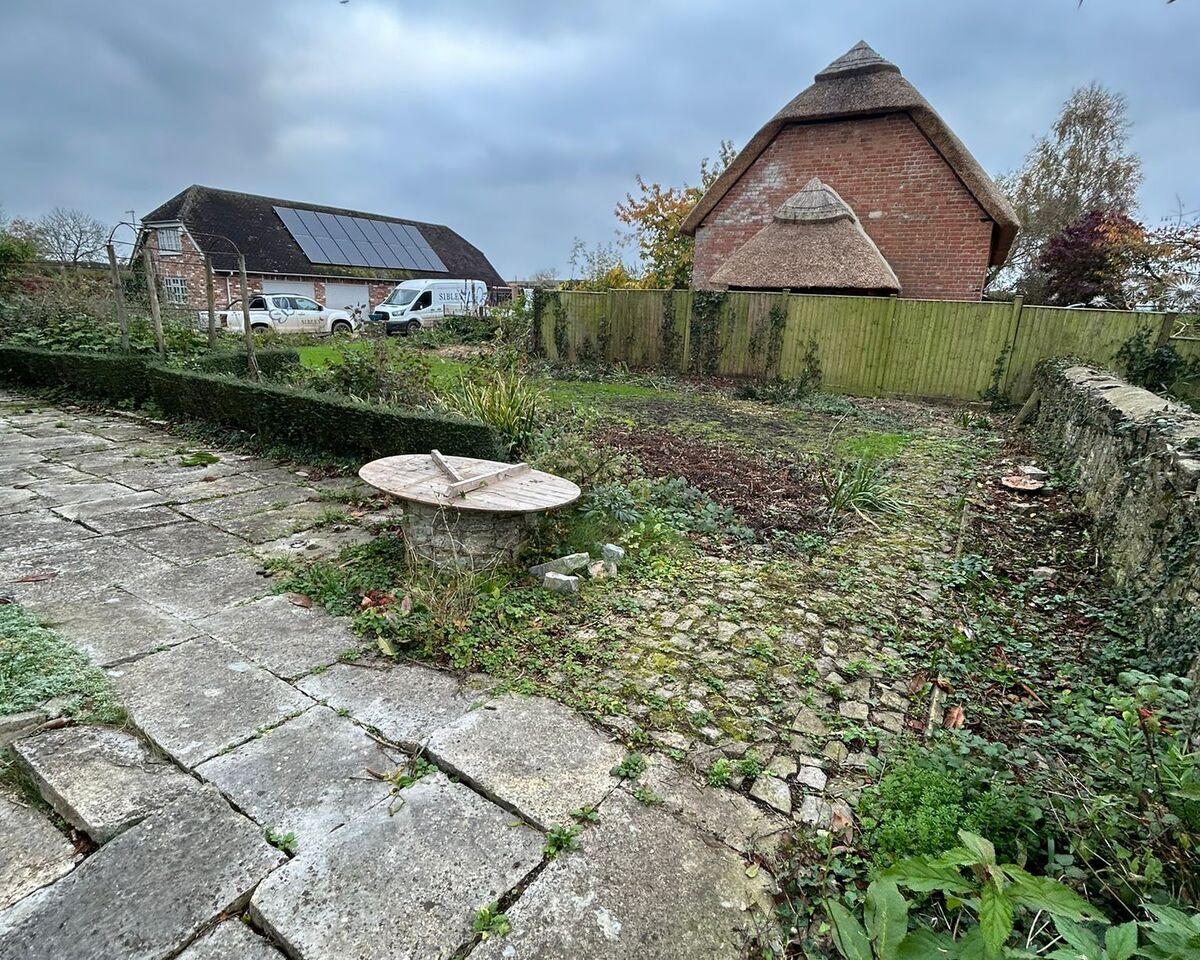 A garden with stone pathways, a circular table, and a barn in the background under cloudy skies.
