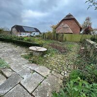 A garden with stone pathways, a circular table, and a barn in the background under cloudy skies.