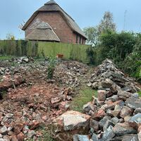 Rubble and debris in a garden with a thatched-roof house in the background.