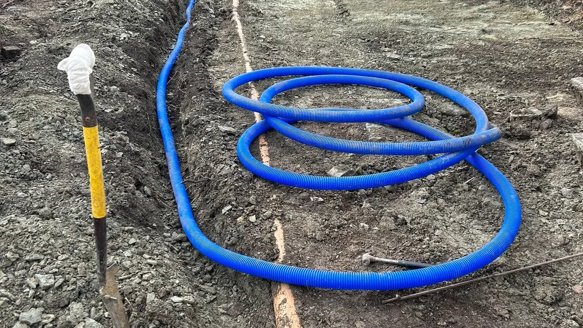 Blue perforated land drain coiled in an open trench across excavated ground beside a house